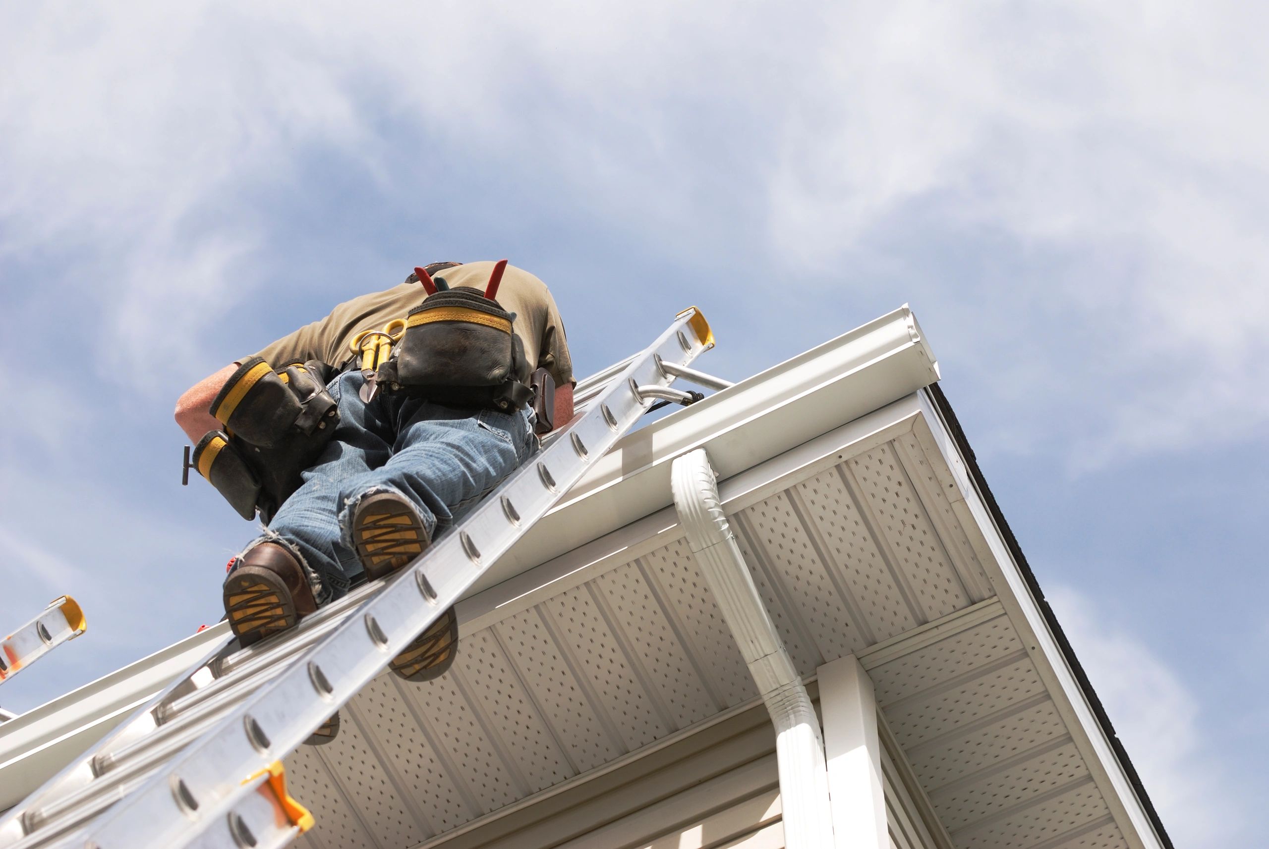 Technician cleaning roof gutters from a ladder